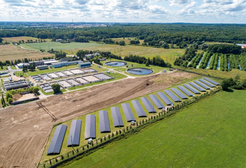 Luftbild einer Kläranlage mit Klärbecken und einer Reihe von Solarmodulen.