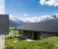 KI-Visualisierung eines mit schwarzen Solarziegeln gedeckten Hauses in Gebirgsregion.
