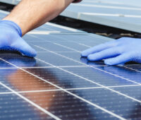 Photovoltaik-Modul und zwei Hände in blauen Handschuhen