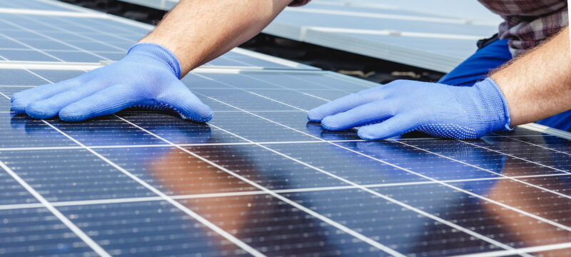 Photovoltaik-Modul und zwei Hände in blauen Handschuhen
