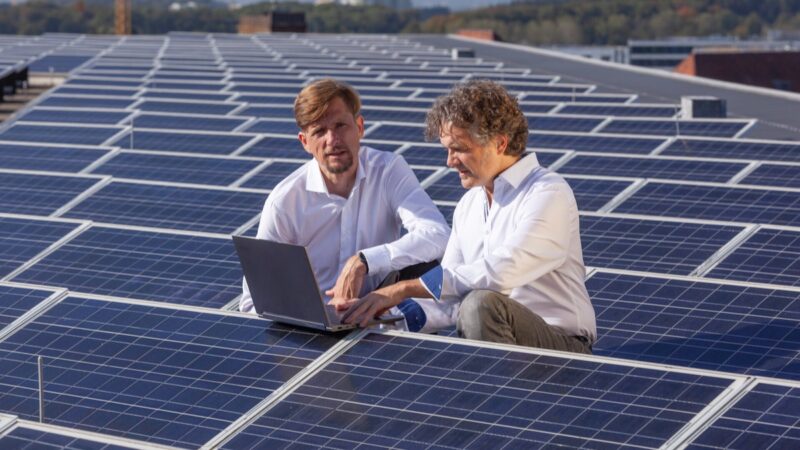 Zwei Männer mit Laptop sitzen zwischen Photovoltaik-Modulen