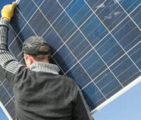 Ein Mann trägt ein PV-Modul, neues Faktenblatt „Repowering von Photovoltaik-Anlagen“.
