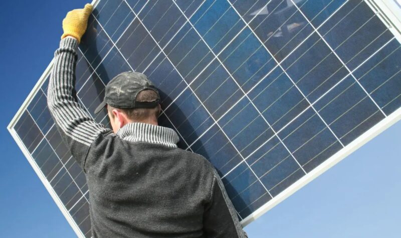 Ein Mann trägt ein PV-Modul, neues Faktenblatt „Repowering von Photovoltaik-Anlagen“.