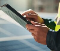 Im Bild ein Mann mit Tablett vor einer PV-Anlage