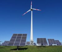 Eine Windenergie-Anlage und mehrere Photovoltaik-Nachführsysteme auf einer Wiese vor blauem Himmel