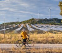 Mensch mit Fahhrad steht auf einem Weg und schaut zu Solarpark und Windenergie-Anlagen. Symbolbild für Photovoltaik und Windenergie in der Region Kastilien und Leon, Spanien.