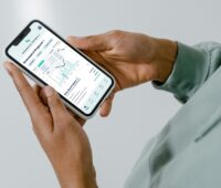 Im Bild Hände, die ein Handy halten, auf der die App von Ostrom mit dem virtuellen Kraftwerk Neogrid AI läuft.