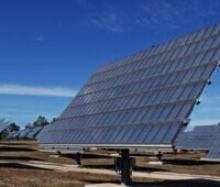 Ein Photovoltaikmodul auf einem Tracker in einem großen PV-Park unter blauem Himmel und auf trockener Erde.