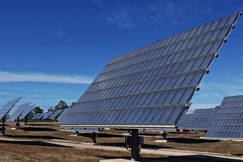 Ein Photovoltaikmodul auf einem Tracker in einem großen PV-Park unter blauem Himmel und auf trockener Erde.