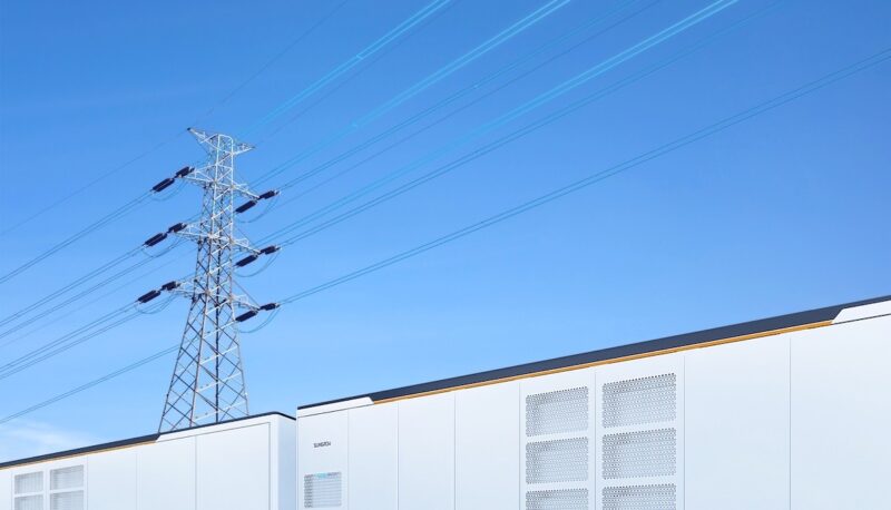 Ein im Vordergrund angeschnittener Batteriespeicher PowerTitan 2.0 in lichtgrau vor blauem Himmel. Im Hintergrund eine Strommast.