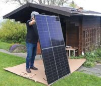 Mann mit Photovoltaik-Modul, Idealo hat Ranking für Balkonkraftwerke aufgestellt.