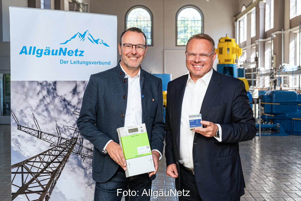 Die beiden Verantwortlichen stehen nach der Vertragsunterzeichnung nebeneinander vor einem Werbebanner von AllgäuNetz. Einer zeigt einen digitalen Zähler.