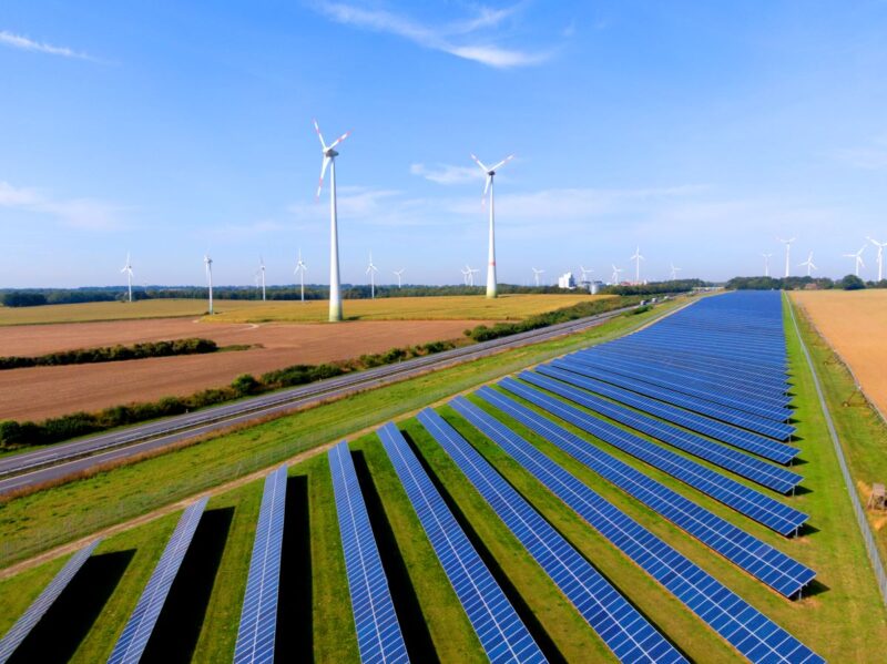 Solarfreifläche und Windenergieanlagen im Flachland bei Sonnenschein.