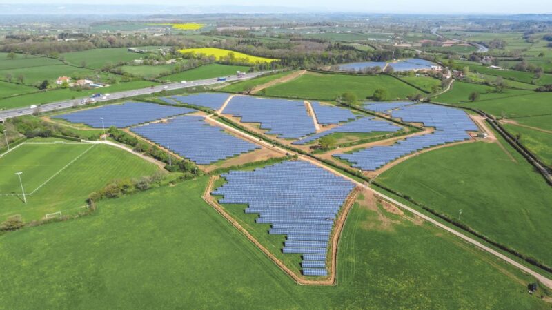 Luftaufnahme zeigt Solarparks umgeben von grünen Feldern entlang einer Autobahn