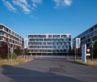 Mehrere moderne vierstöckige Bürogebäude unter blauem Himmel.