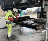 Ein Monteur entfernt die Autobatterie eines Unfallwagens, das RAL Gütezeichen Havarie Elektromobilität und Energiespeicher soll für einen sicheren Umgang mit Batterien im Schadensfall sorgen.