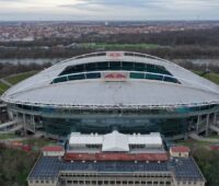 Das Stadion in Leipzig aus der Luft. Im Vordergrund ein gründerzeitliches Gebäude mit Solarpaneelen auf dem Dach.