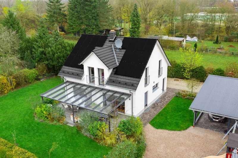 Blick auf ein freistehendes Einfamilienhaus mit Schrägdach, auf dem schwarze Module installiert sind.