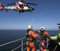 Ein Rettungshubschrauber und Menschen auf einem Schiff, RWE übt Rettung im Offshore-Windpark.