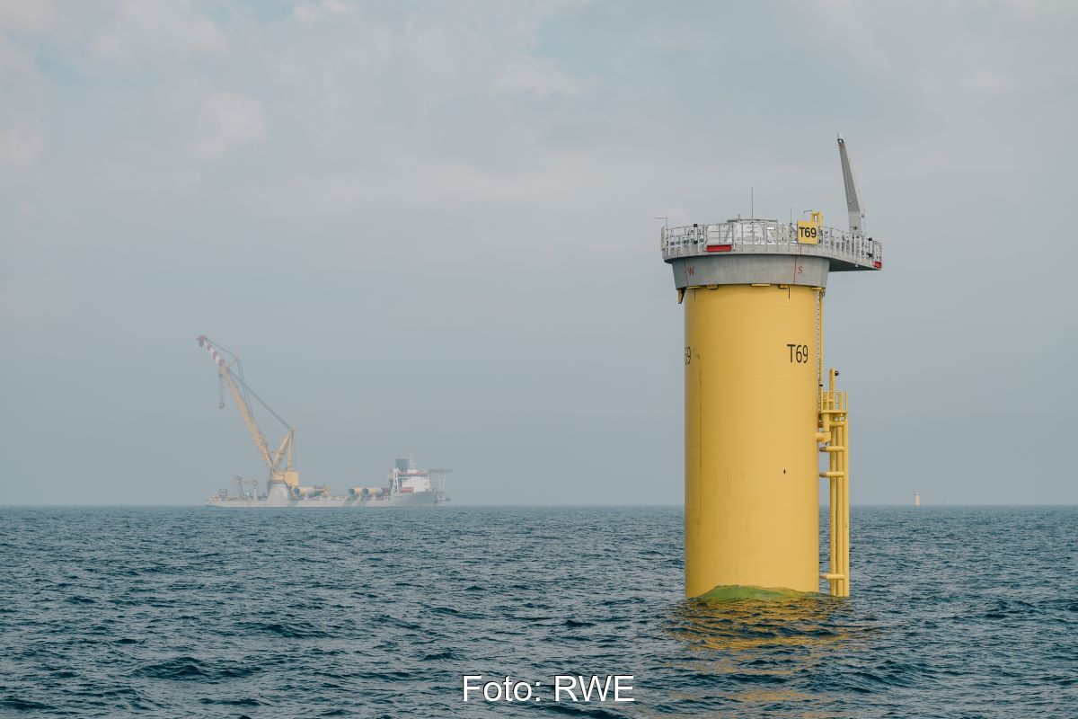 Fundament für Offshore-Windenergieanlage, das aus dem Wasser ragt - im Hintergrund Transportschiff.