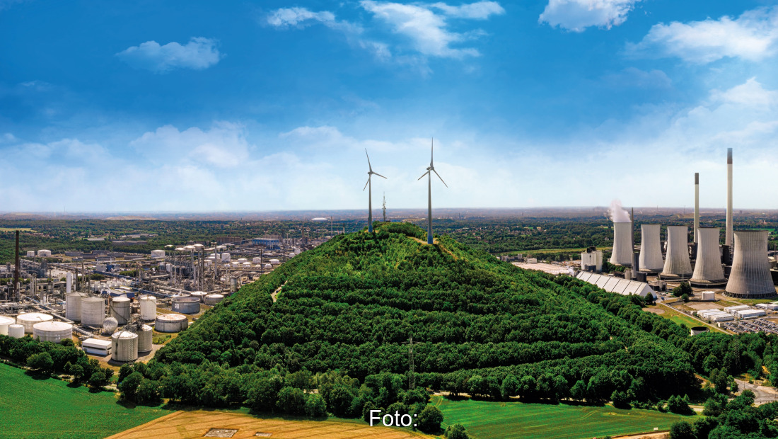 Blick in die Landschaft aus Vogelperspektive: links Stadt, Mitte Wald mit Windrädern, rechts Raffinerie vor blauem Himmel.