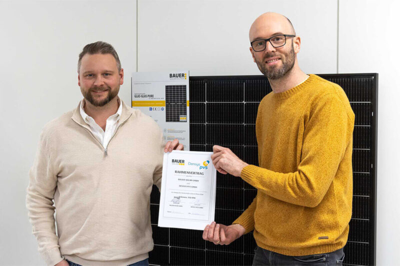 Andreas Bauer und Steffen Binzel halten zusammen den neu geschlossenen Rahmenvertrag in Papierform hoch. Im Hintergrund ist ein Bauer-Modul zu sehen.