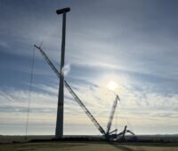 Vor einer milchigen Sonne finden Arbeiten mit einem Kran an einer Windenergieanlage statt.