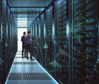 Zwei Männer im Gang eines Rechenzentrums zwischen Computer- oder Speicher-Racks hinter Glas, wobei das Foto im bläulichen Licht an eine Science-Fiction-Umgebung erinnert.
