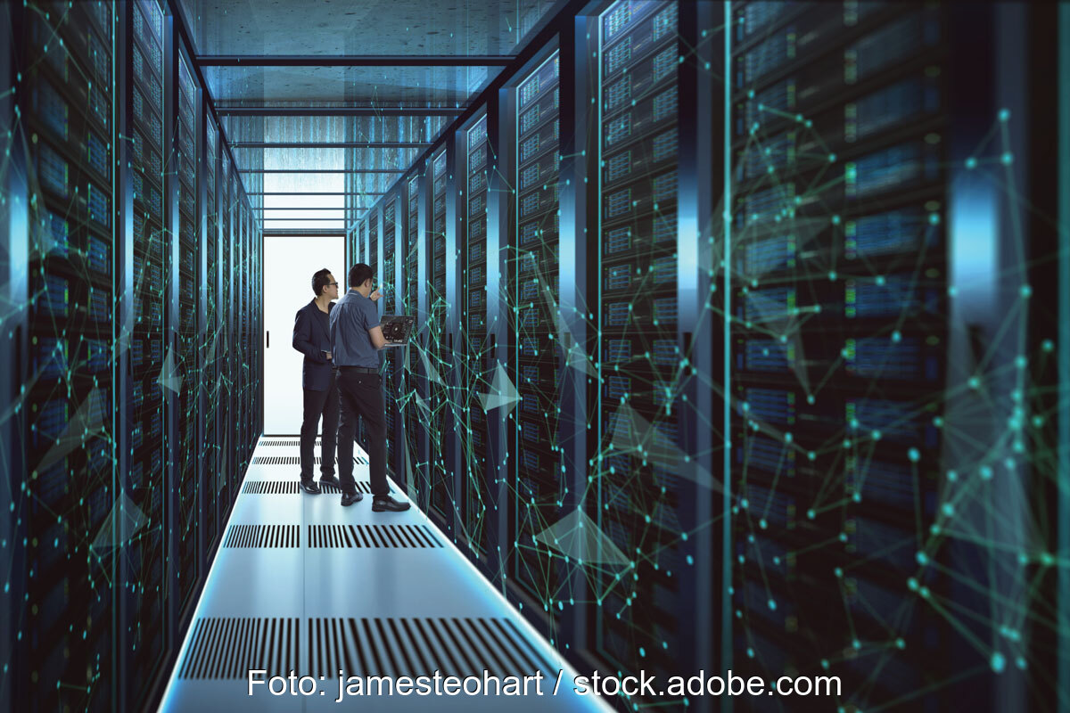 Zwei Männer im Gang eines Rechenzentrums zwischen Computer- oder Speicher-Racks hinter Glas, wobei das Foto im bläulichen Licht an eine Science-Fiction-Umgebung erinnert.