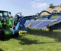 Reinigung von Photovoltaik-Anlagen: ein Fahrzeug fährt mit einer großen Bürste über eine Modulreihe.