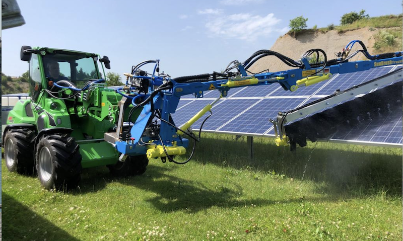 Reinigung von Photovoltaik-Anlagen: ein Fahrzeug fährt mit einer großen Bürste über eine Modulreihe.