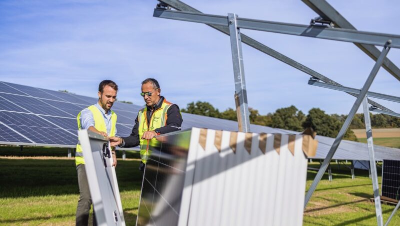 Zwei Männer mit einem Paket Solarmodule neben einem Freiflächen-Montagegestell im Solarpark - Symbolbild für Revamping