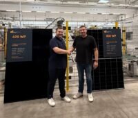 Die beiden Verantwortlichen stehen händeschüttelnd in der Produktionshalle für 500-W-Back-Contact-Module bei Sonnenfarbrik.