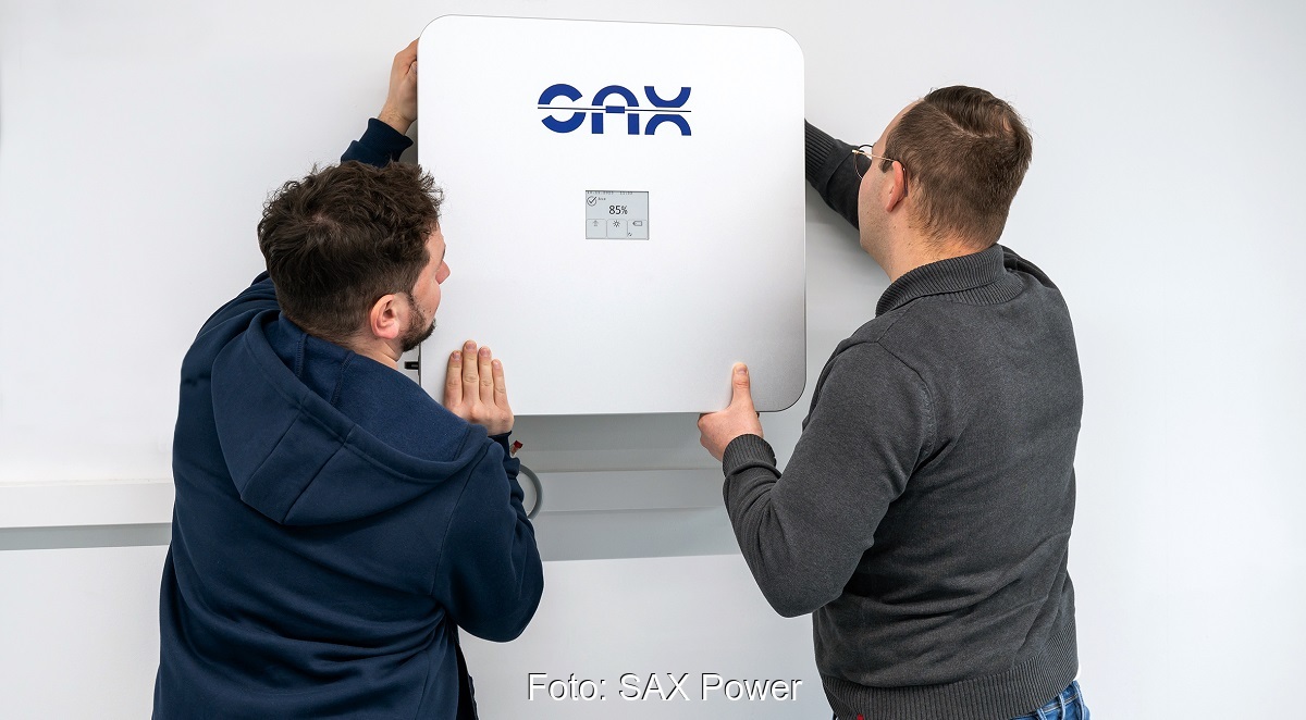 Zwei Männer hängen einen Der SAX Power PV-Speicher an die Wand.