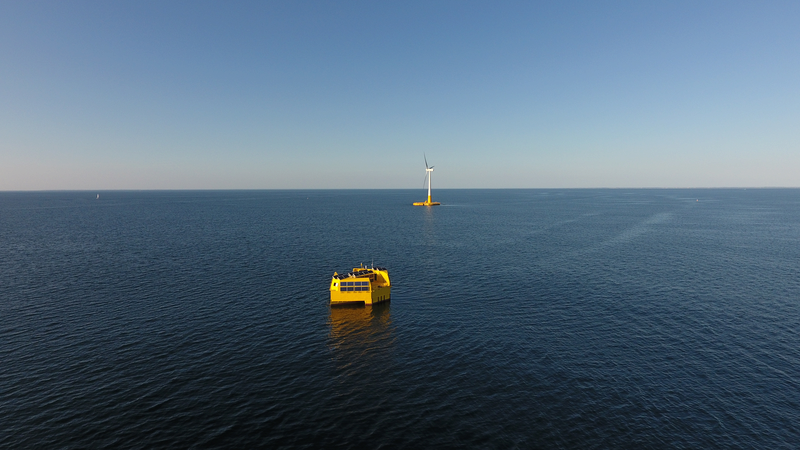 Blick übers Meer, ein gelbes Boot und ein Offshore-Windrad