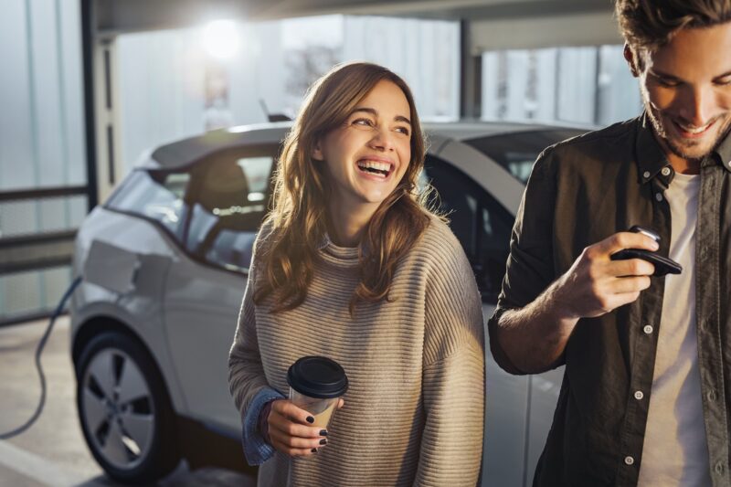 Zu sehen sind zwei Menschen mit einem E-Auto im Hintergrund, die die Senec.Cloud to go nutzen könnten.