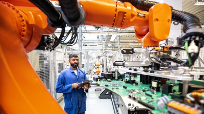 Im Bild ein Arbeiter unter einem Roboterarm in der neuen SMA Elektronikfertigung.