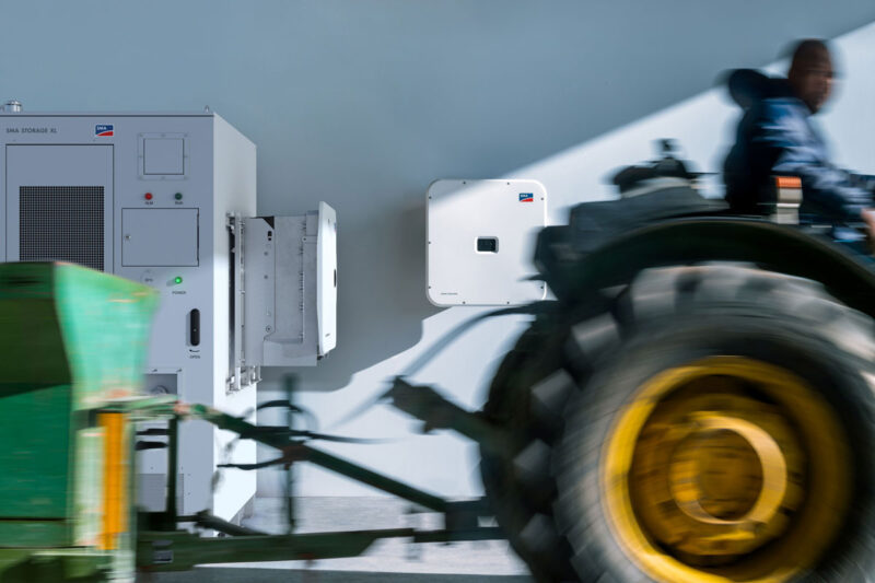 Traktor passiert eine Kombination von weißem SMA-Speicher und -Wechselrichter vor einer weißen Wand.