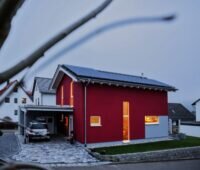Ein beleuchtetes Haus mit Solaranlage auf dem Dach und einem Auto unter Carport.