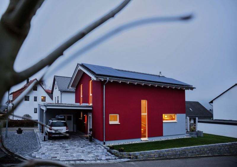 Ein beleuchtetes Haus mit Solaranlage auf dem Dach und einem Auto unter Carport.