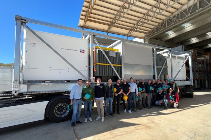 LKW mit großen elektrotechnischen Komponenten und SMA-Mitarbeitern davor.