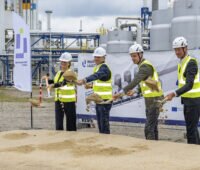 Vier Personen mit weißen Schutzhelmen und neongelben Warnwesten beim Spatenstich für die SOEC-Testanlage im Industriepark Lausitz in Schwarzheide.