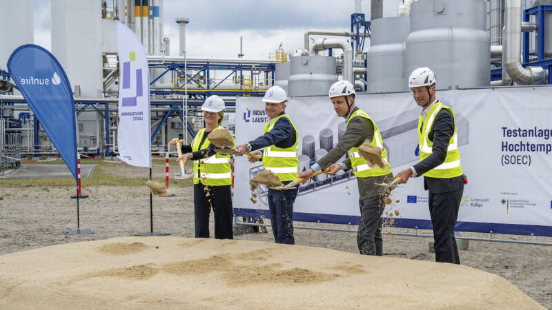 Vier Personen mit weißen Schutzhelmen und neongelben Warnwesten beim Spatenstich für die SOEC-Testanlage im Industriepark Lausitz in Schwarzheide.