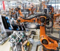 Ein oranger Roboter schwenkt ein Solarmodul in einer Fabrikhalle