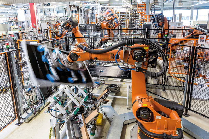 Ein oranger Roboter schwenkt ein Solarmodul in einer Fabrikhalle