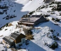 Eine Hüttenanlage in den Alpen mit Solarmodulen auf den Dächern und Schneeumgebung
