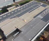 Das Dach eines Gewerbebetriebes wird eine Glas-Glas-Photovoltaikanlage installiert.. Es ist mit Gestellen belegt, auf denen die ersten dunklen Solarmodule installiert wurden.