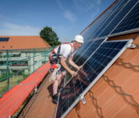 Ein Monteur auf einem Schrägdach installiert Solarmodule.