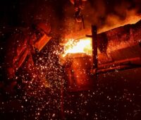 Ein Arbeiter im Schutzanzug bei der Metallschmelze mit glühenden Funken.