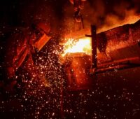 Ein Arbeiter im Schutzanzug bei der Metallschmelze mit glühenden Funken.